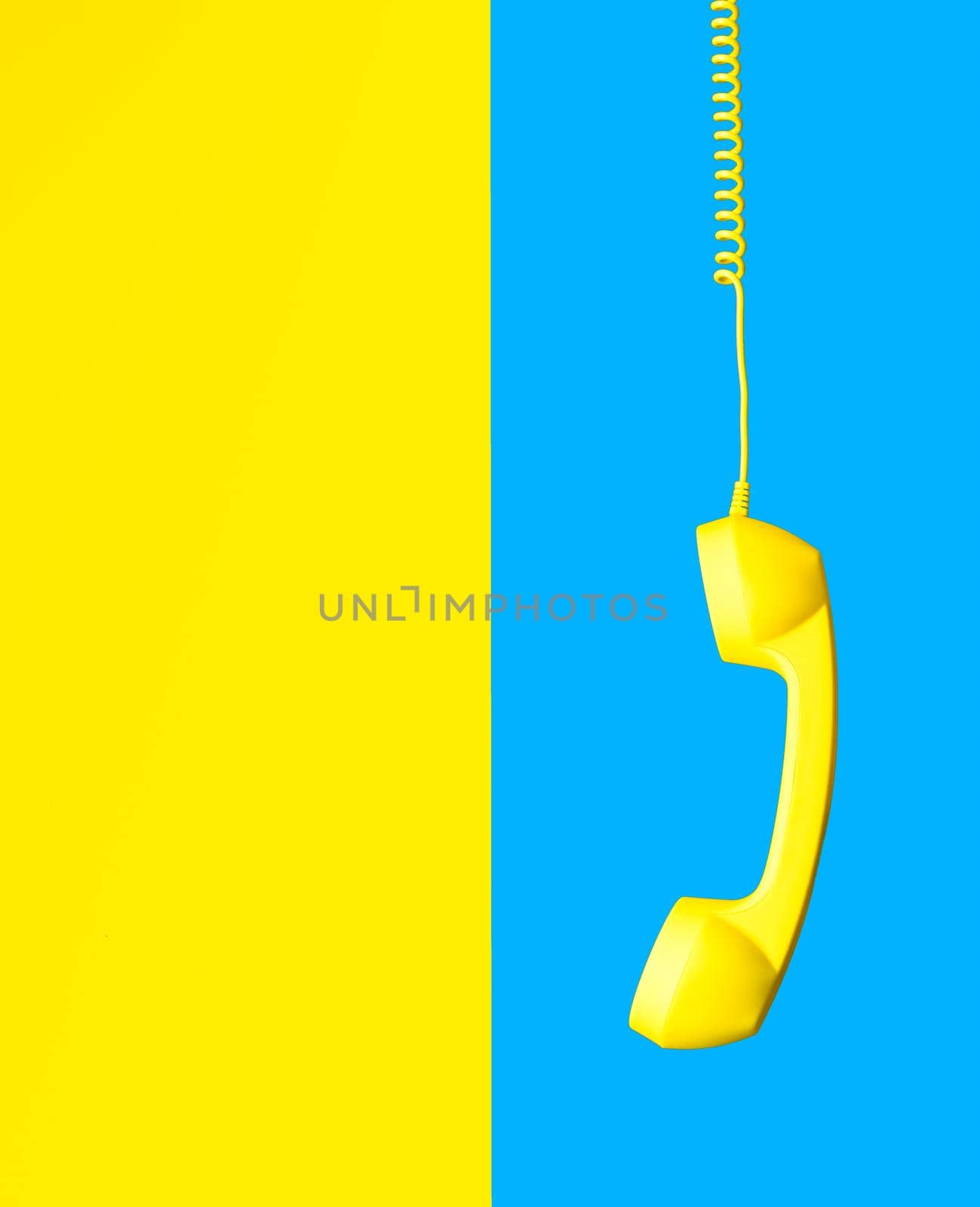yellow retro phone hanging on spiral cord on background split in half in sky blue and yellow