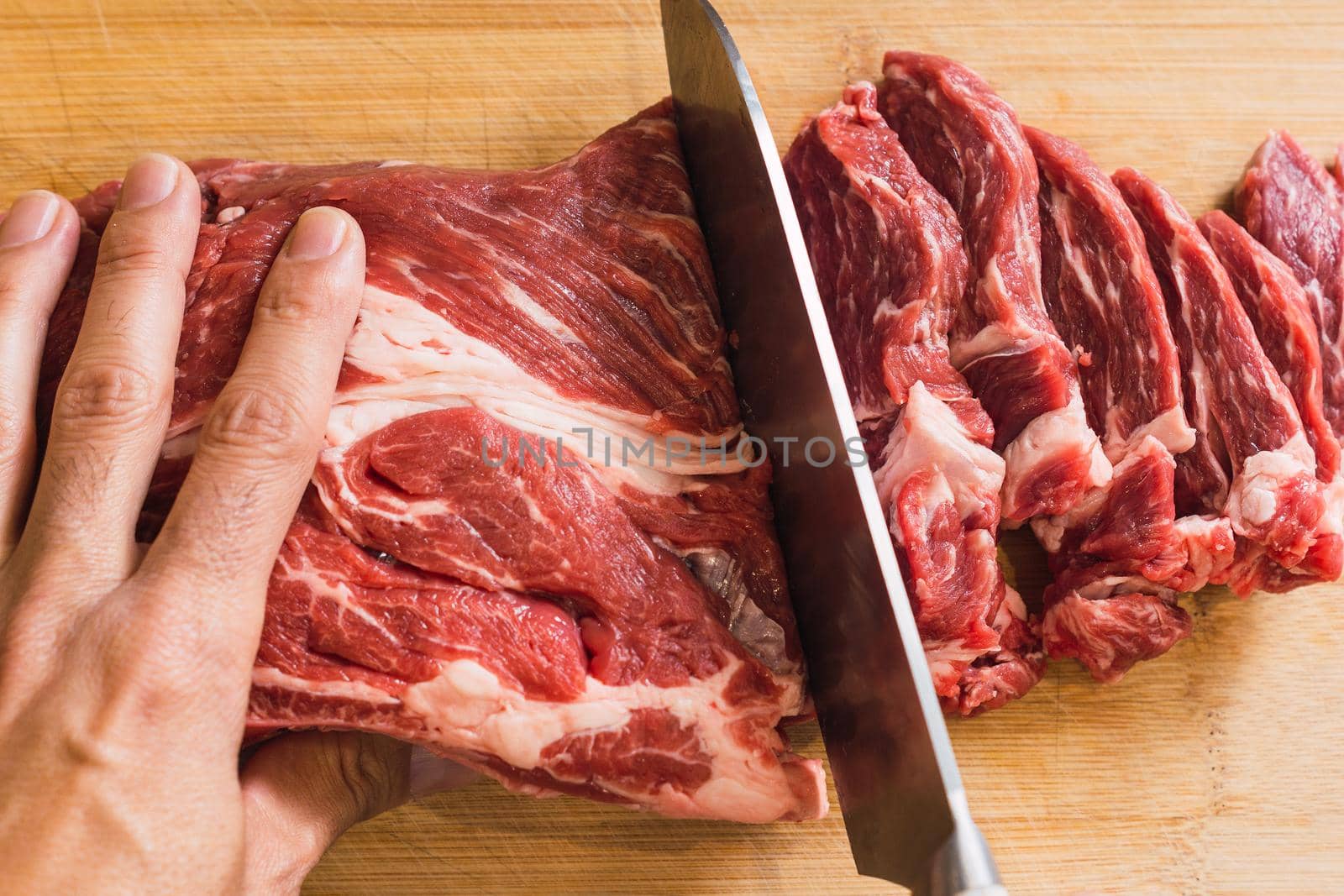 hand and knife filleting a piece of fresh red meat on a wooden board illuminated with natural light