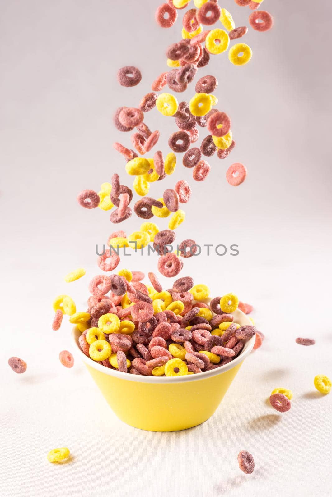 colored cereal rings falling into a yellow bowl on white background with soft side lighting