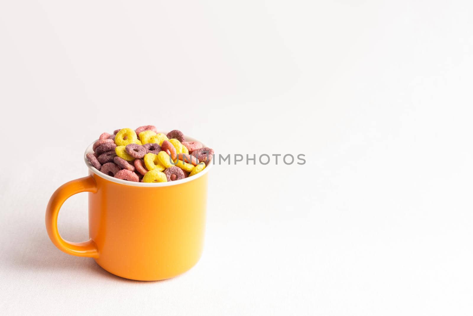 orange cup on white background filled with colorful cereal rings with soft side lighting