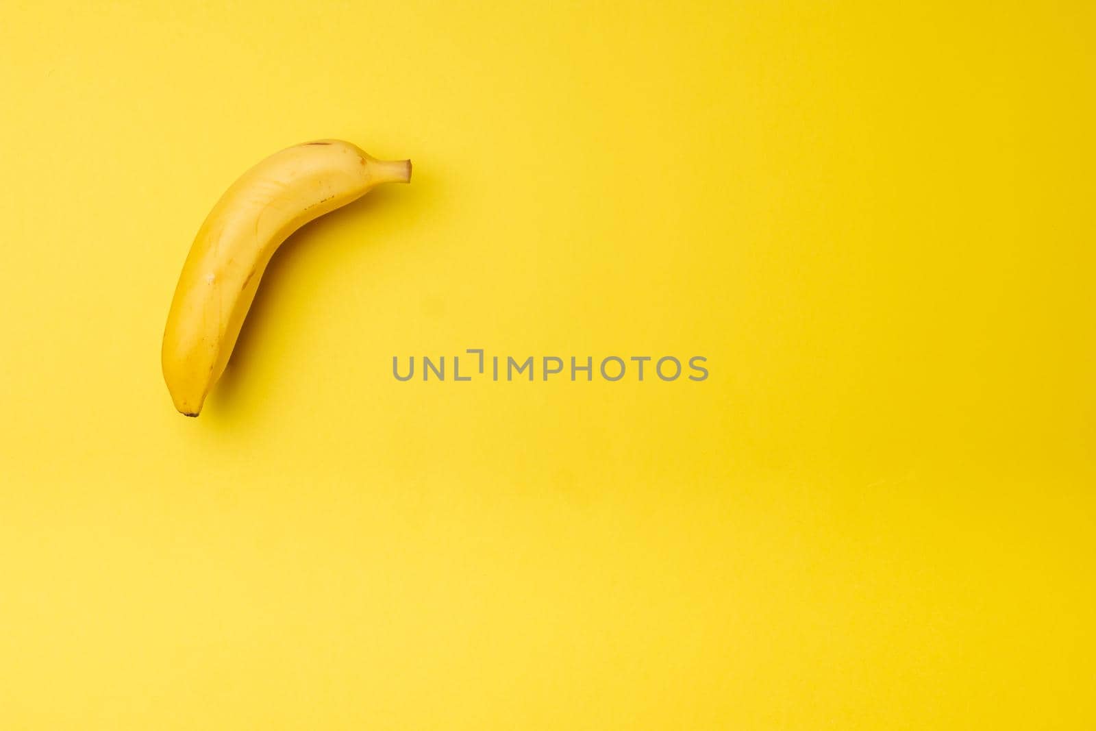 a ripe banana on a yellow background in the upper left corner with soft light from the side