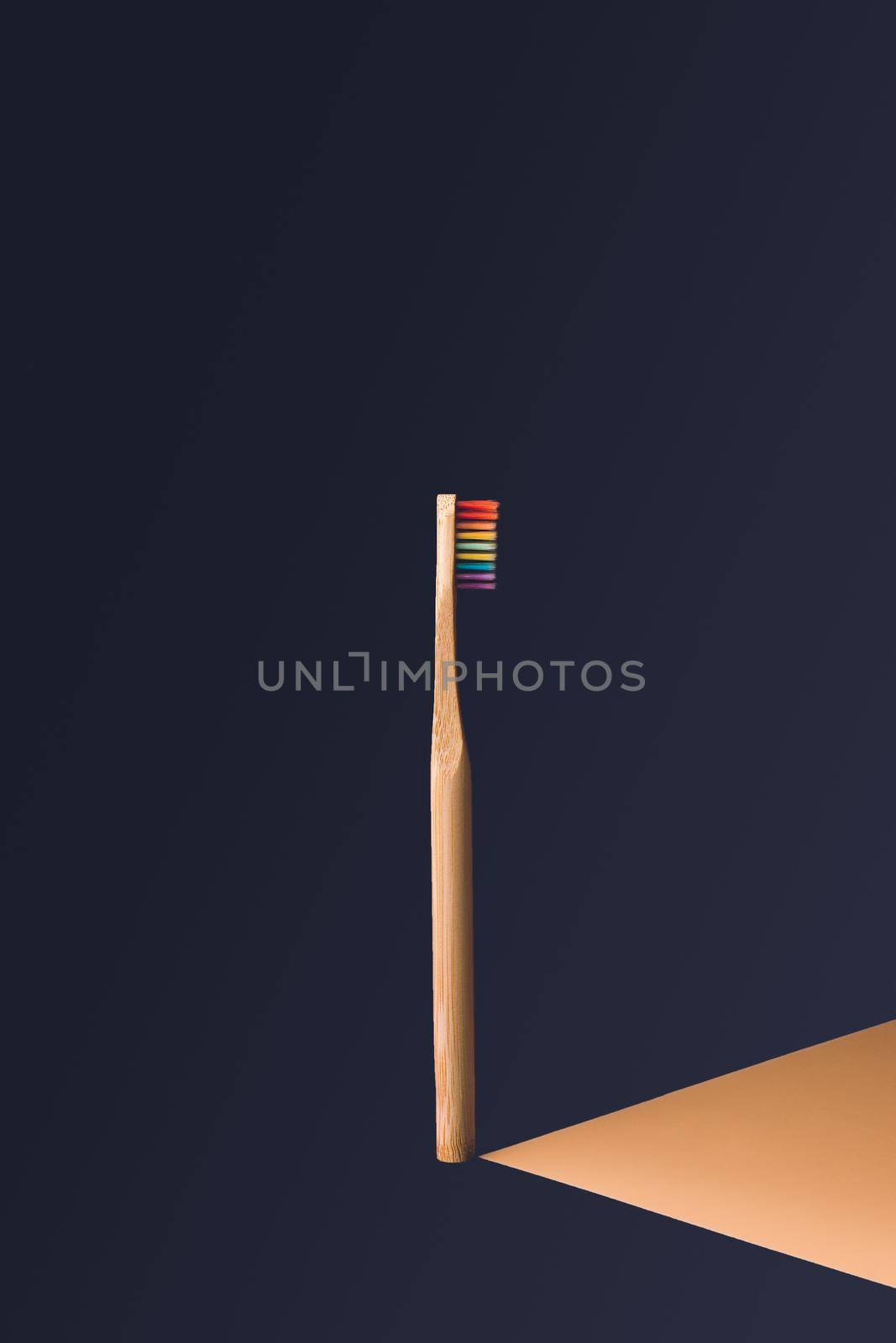 vertical rainbow wooden toothbrush in center of image with dark blue background with orange shadow effect projected to the right