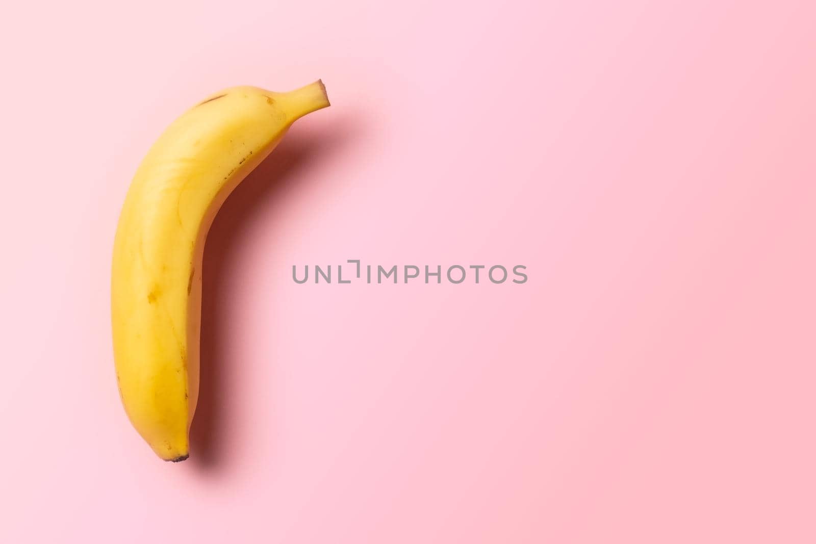 a ripe banana in the upper left corner on a pink background with soft side lighting