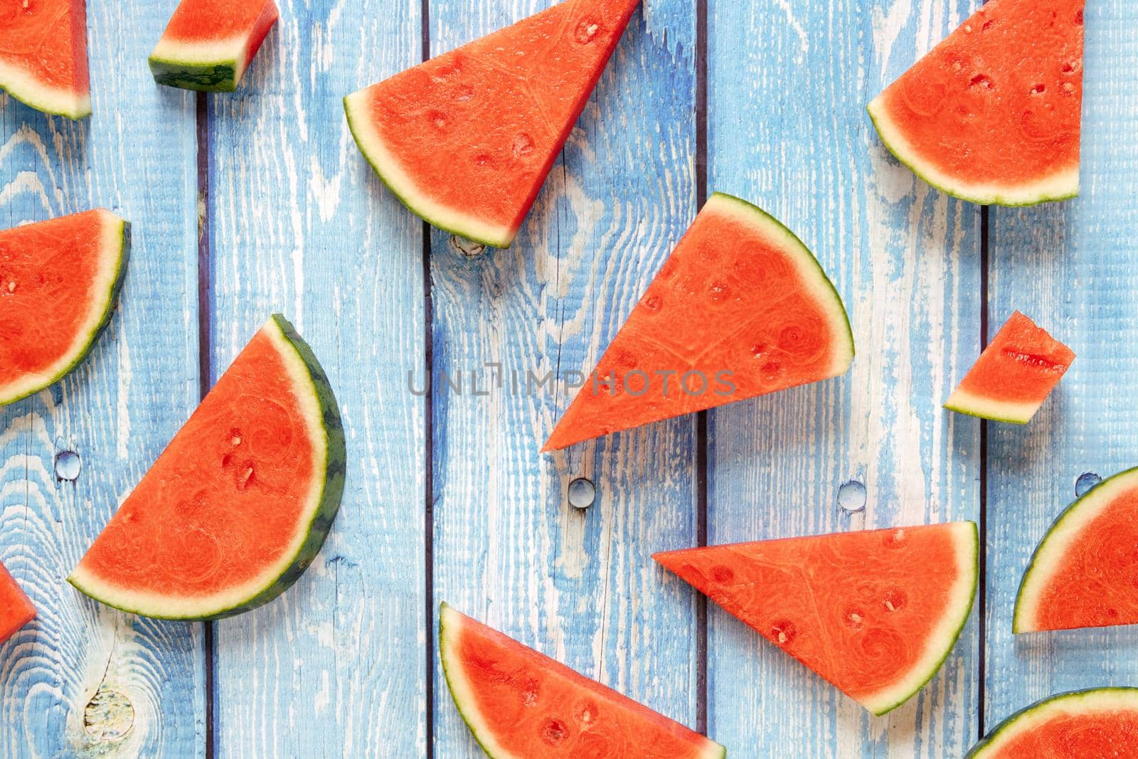 triangular pieces of watermelon on a blue wooden table by jatmikaV