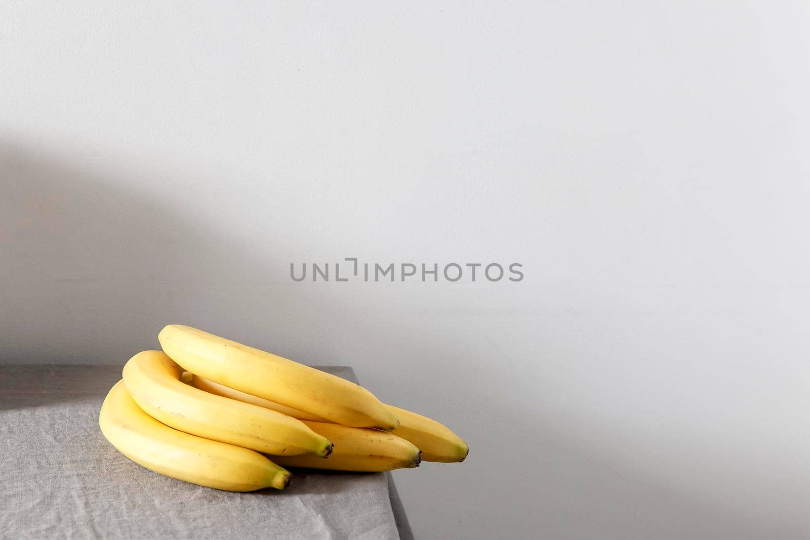 A bunch of bananas on a beige table against a white wall. Scandinavian style. Minimalism. Place for text by elenarostunova