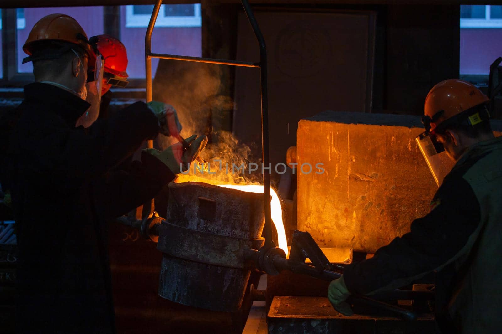 three workers with ladle pouring molten steel into mold in Tula, Russia - February 12, 2020