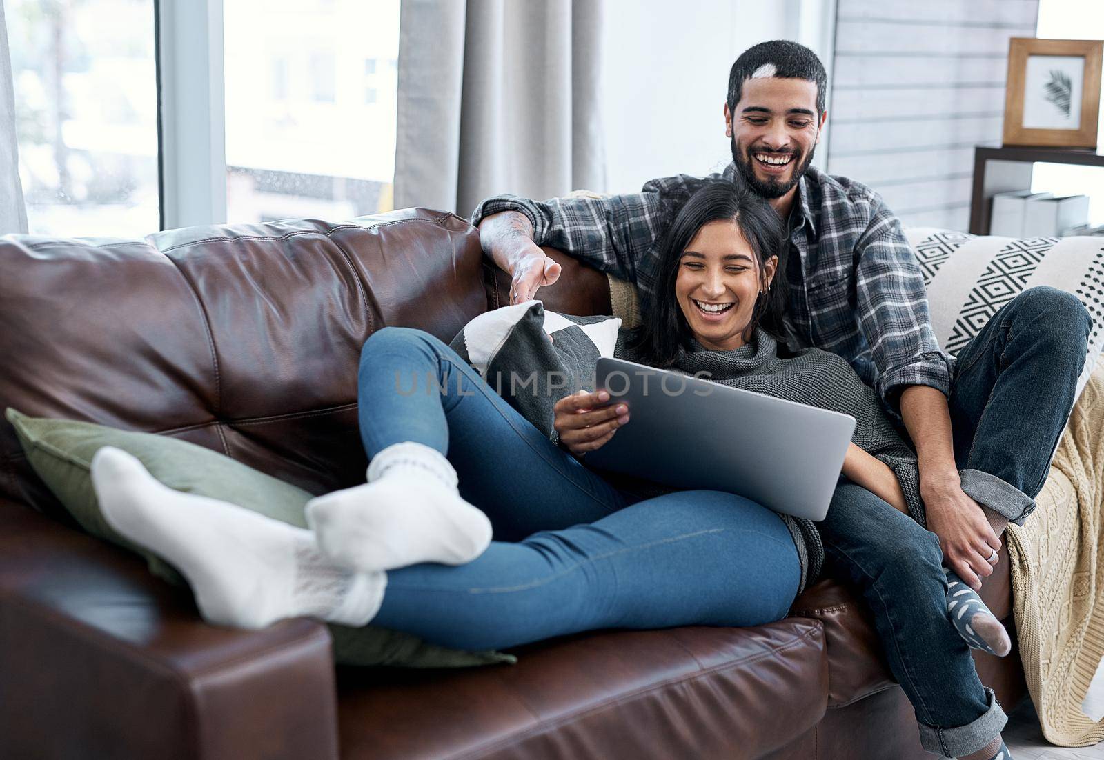 Romance isnt always a fancy date at a restaurant. Shot of a young couple using a laptop while relaxing on the sofa at home. by YuriArcurs