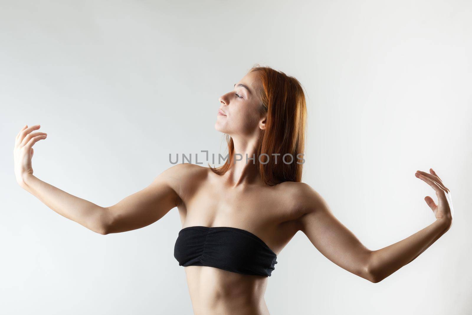 Beautiful girl with burnt orange hair stretching and making ballet pose. Studio portrait on gray background.