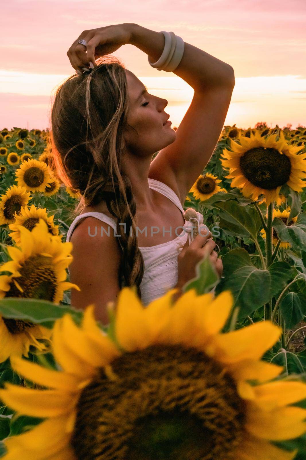 Beautiful middle aged woman looks good in a hat enjoying nature in a field of sunflowers at sunset. Summer. Attractive brunette with long healthy hair