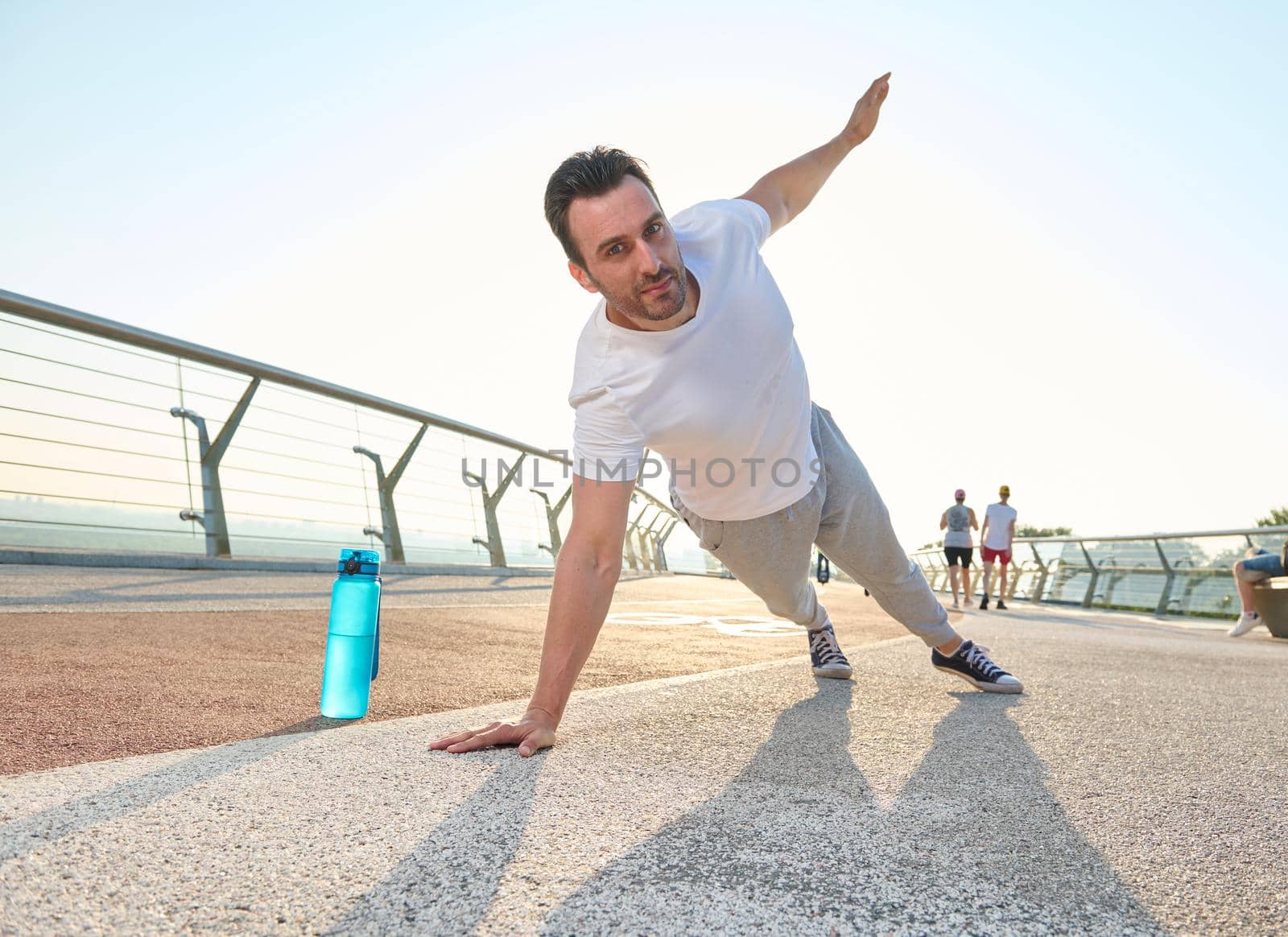 Middle aged European athlete sportsman doing push-ups, exercising on the glass city bridge at dawn. Bottle with water on the treadmill. Sport, active and healthy lifestyle concept