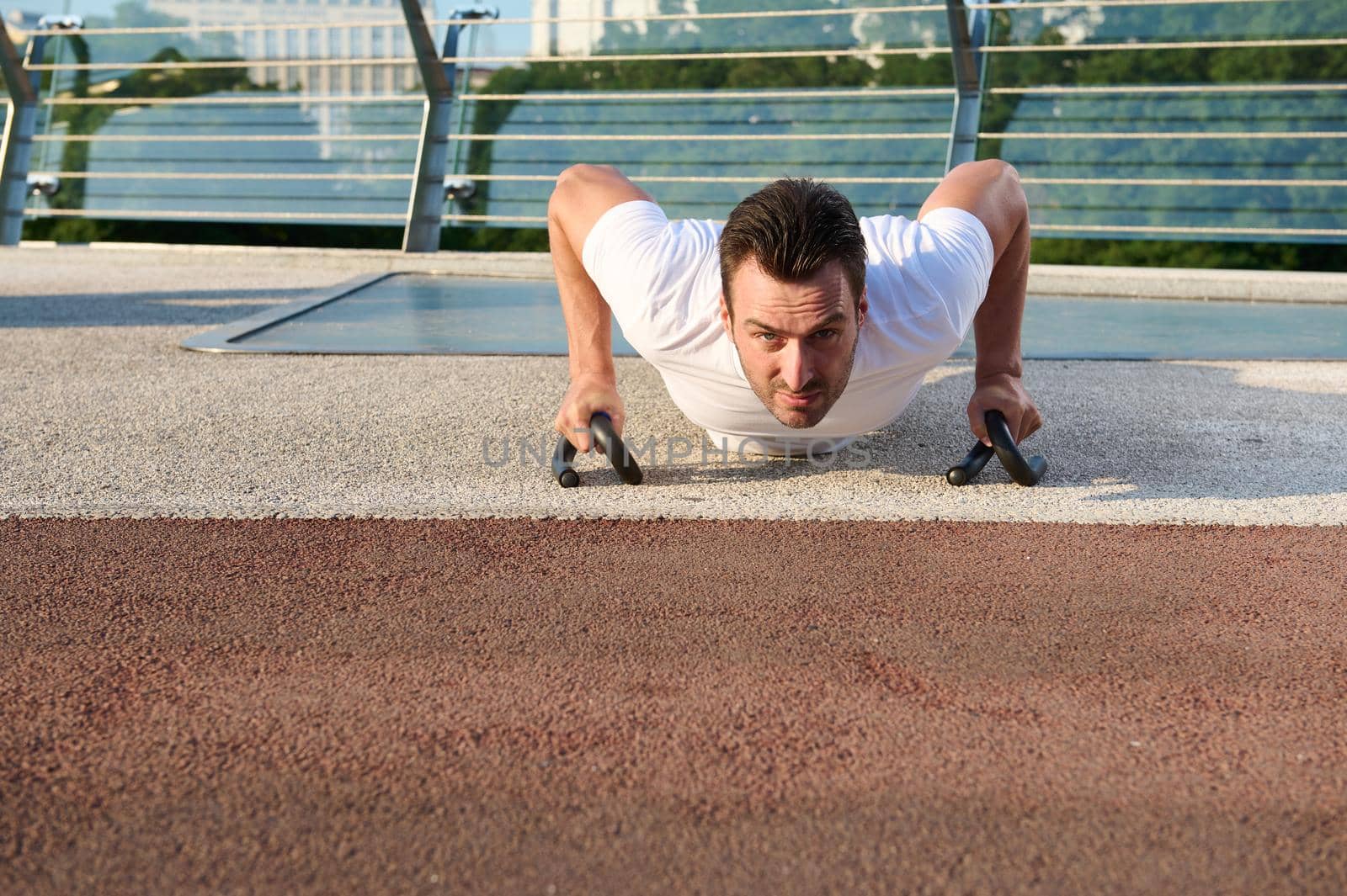 Front view of a handsome middle aged Caucasian man, determined sportsman doing push-ups, pumping chest and shoulders muscles during morning workout outdoor. Keep your body fit and enjoy summer moments