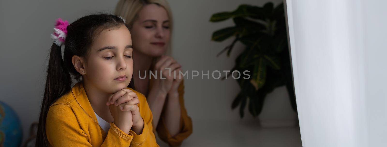 Mother and her daughter reading from bible and praying in their knees near the bed.