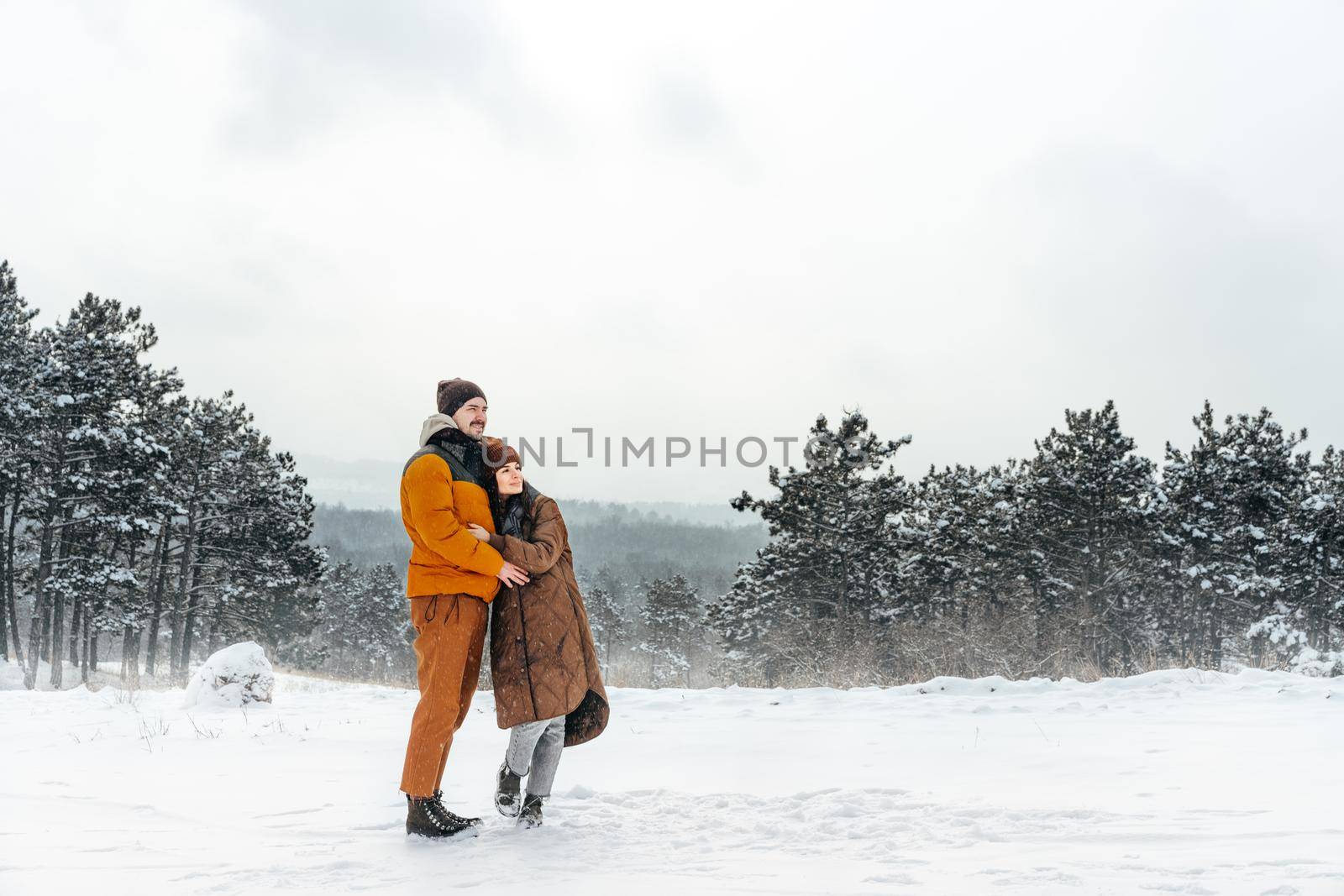 Young couple in love outdoor in snowy winter forest having a walk
