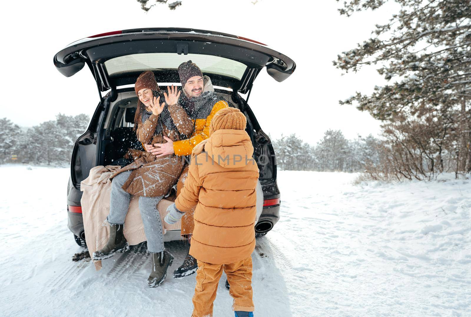 Lovely smiling couple sitting in car trunk in winter forest by Fabrikasimf