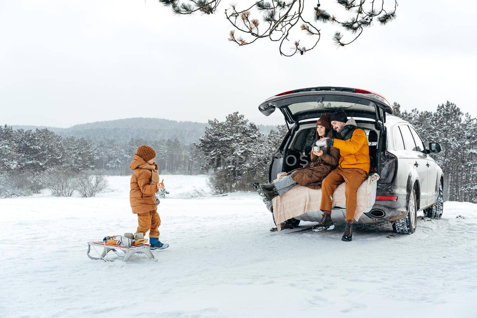 Winter portrait of a family sit on car trunk enjoy their vacation in snowy forest