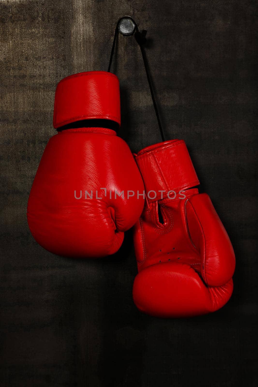 Close up pair of red leather boxing gloves hanging over black wall with copy space