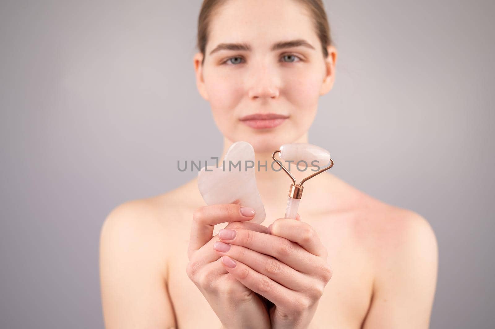 Caucasian woman holding pink roller massager and gouache scraper on white background