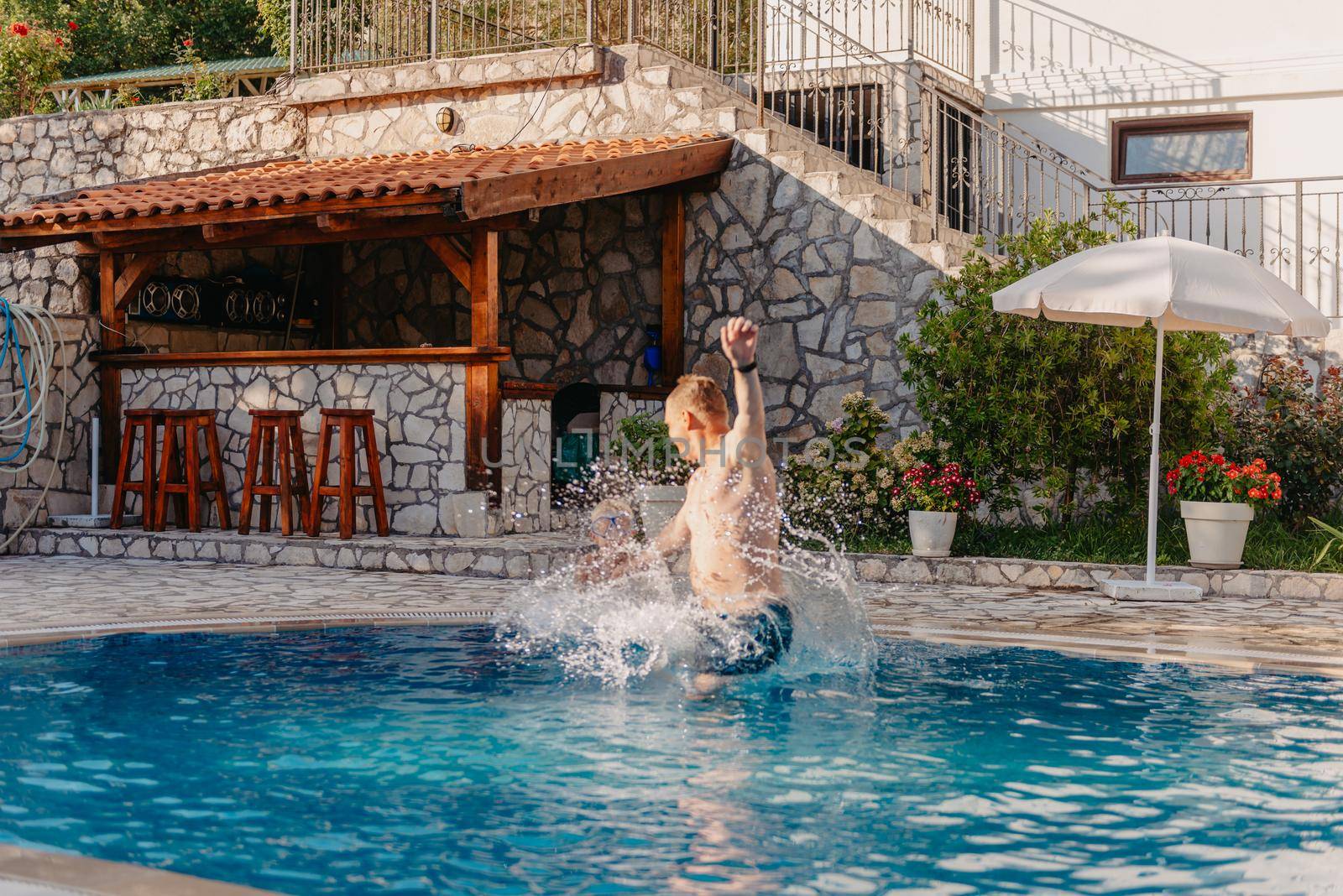 Excited boy in googles jumping in water from shoulders of his father standing in swimming pool