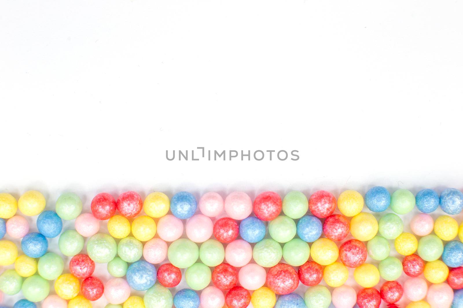 Multi-colored round glossy balls of sugar confectionery topping lie at the down on a white background.Copy space