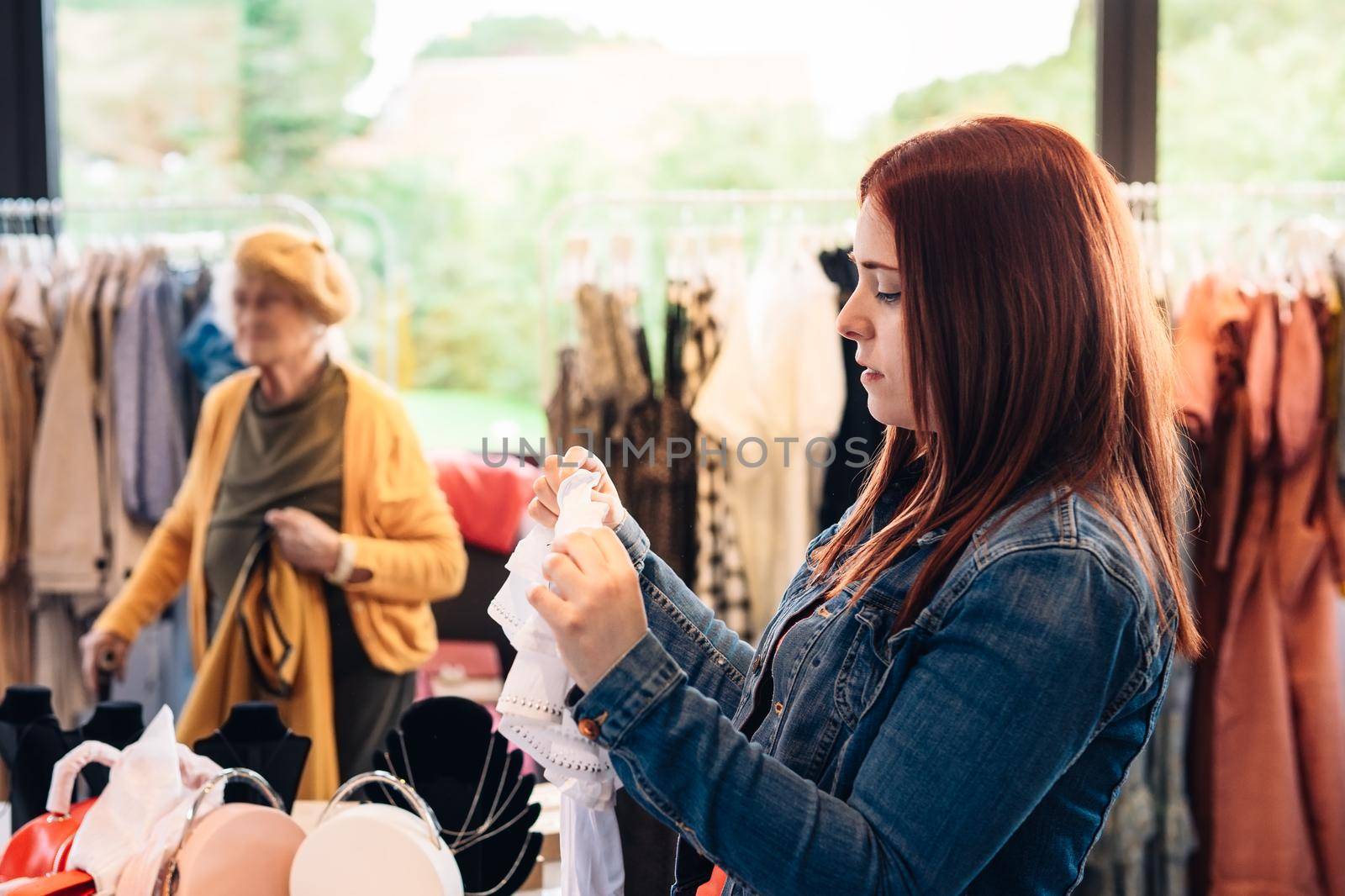 young woman red hair looking at clothes in a fashion shop, deciding what to buy, shopping concept. concept ocio. by CatPhotography