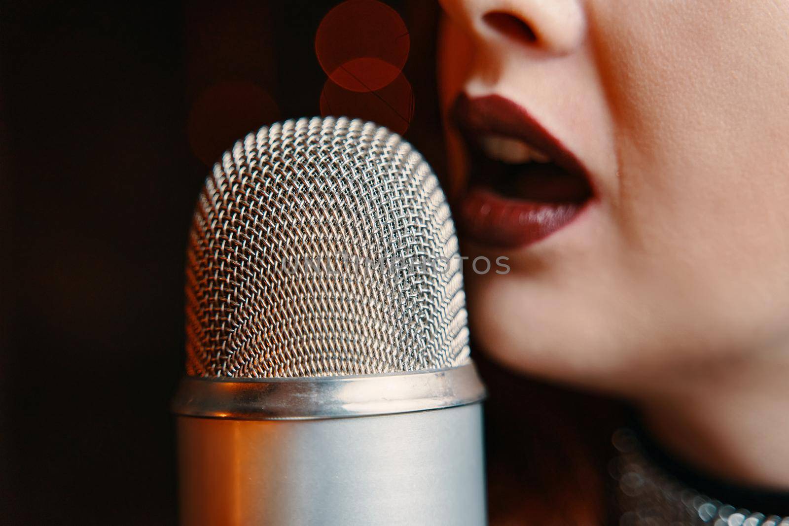 Woman singer with disco mic on bokeh light background. Copy space for gig posters. Close-up of female's lips painted with burgundy lipstick and retro microphone.
