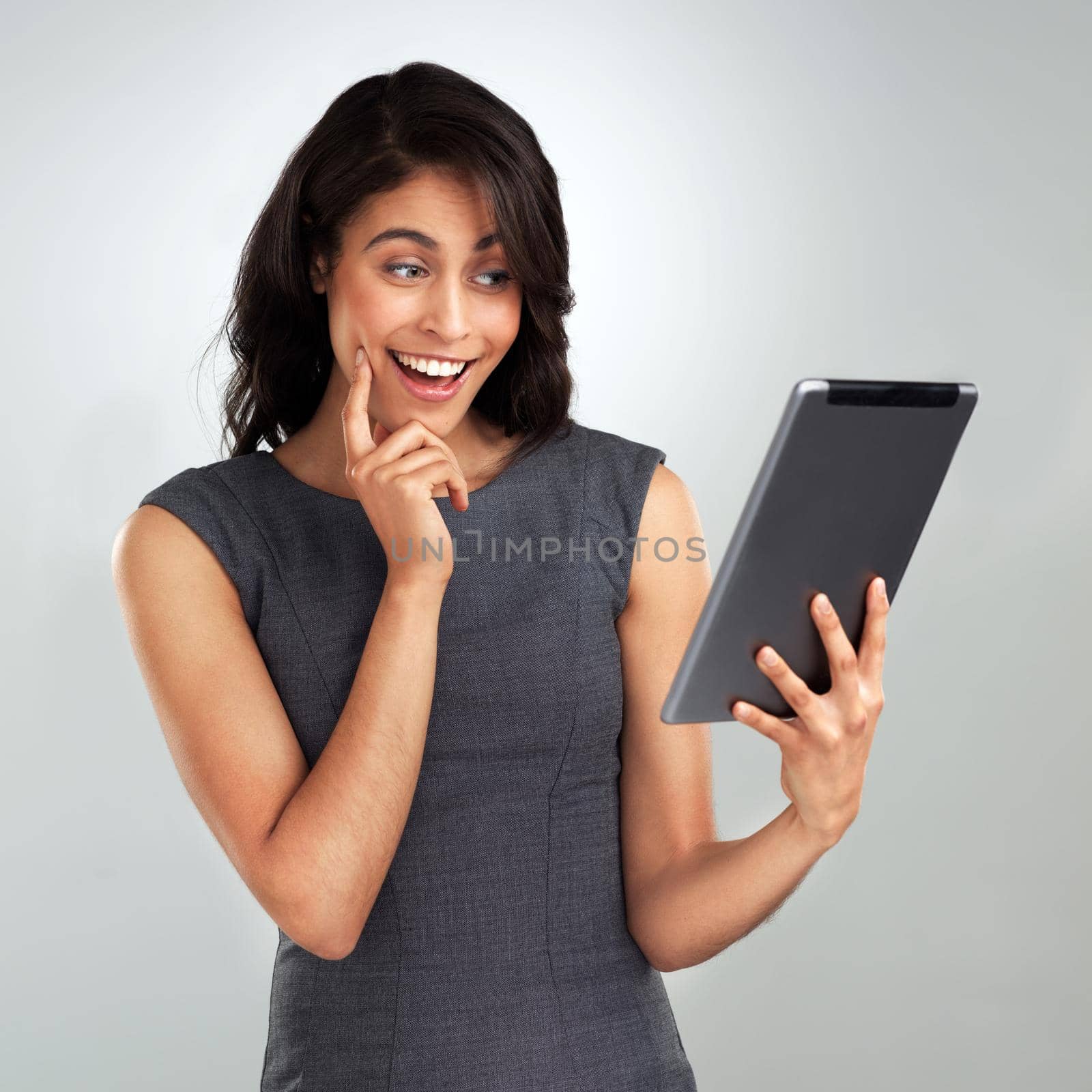Shot of a beautiful young woman using a digital tablet while standing against a grey background.