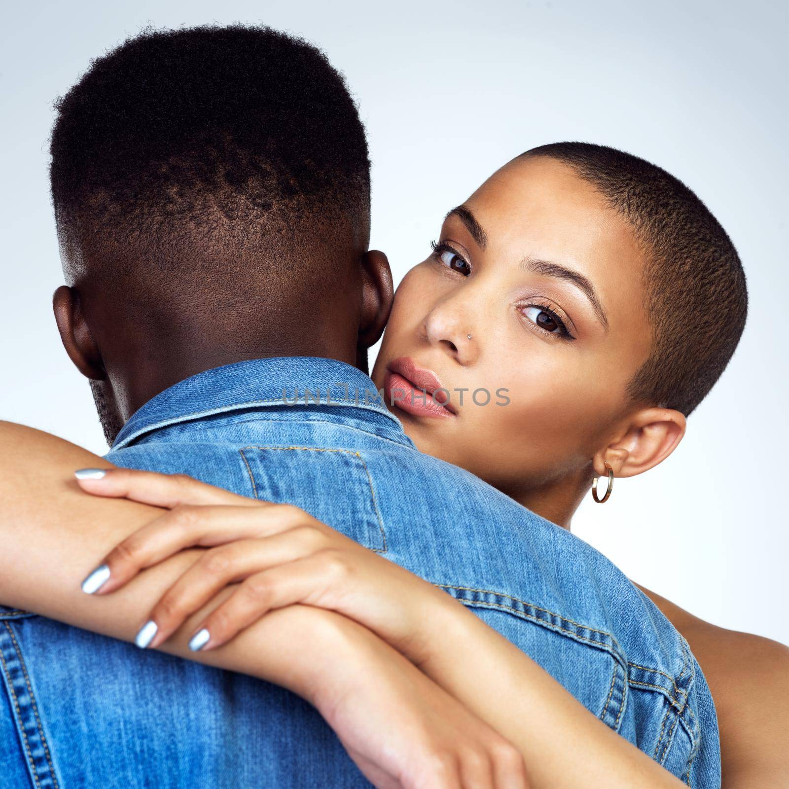 Studio shot of a young couple embracing each other against a grey background.