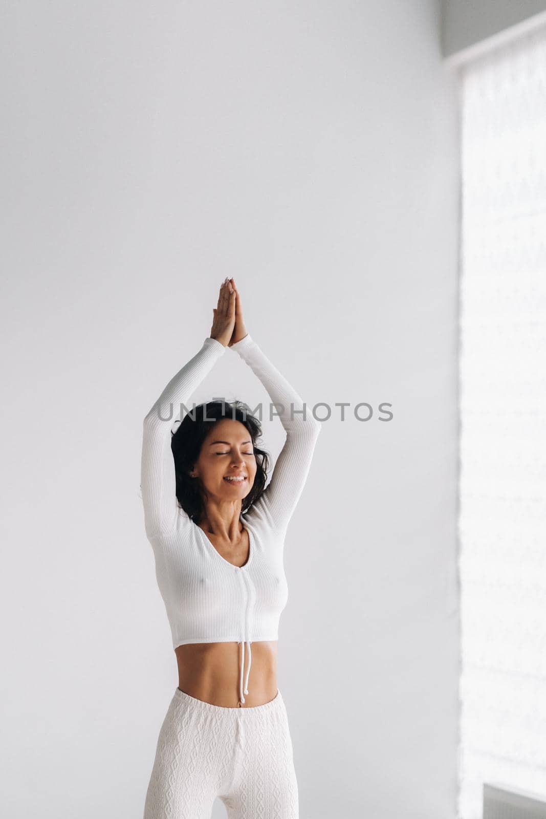 a female yogi in white clothes with her hands up meditates in the Yoga hall.