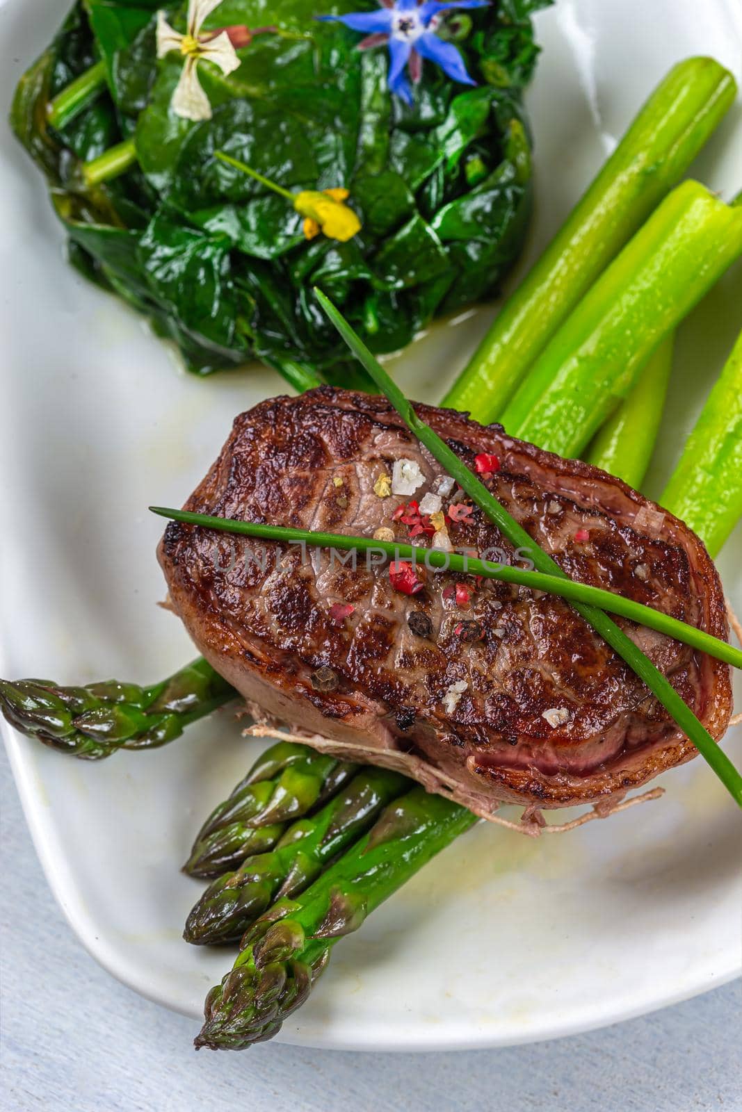 Top view of a grilled tournedos accompanied by spinach and asparagus.