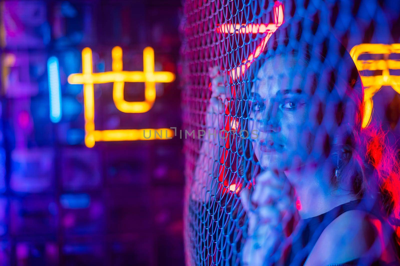 Caucasian woman in neon studio behind chain-link mesh. by mrwed54