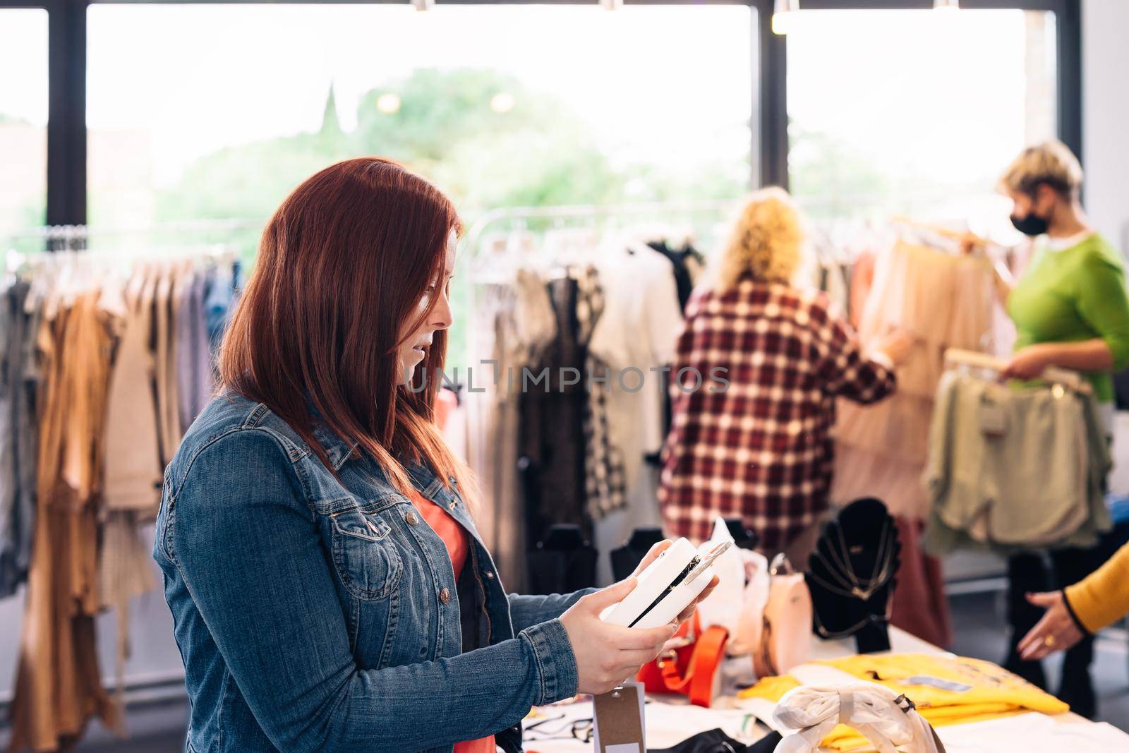 young woman looking at a handbag from the shelf to buy it, in a fashion shop. shopping concept. by CatPhotography