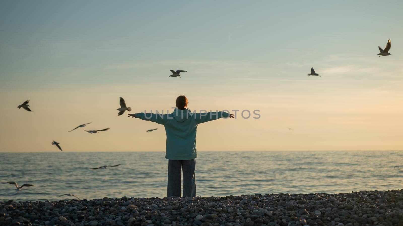 Caucasian woman spread her arms like wings on the seashore at sunset