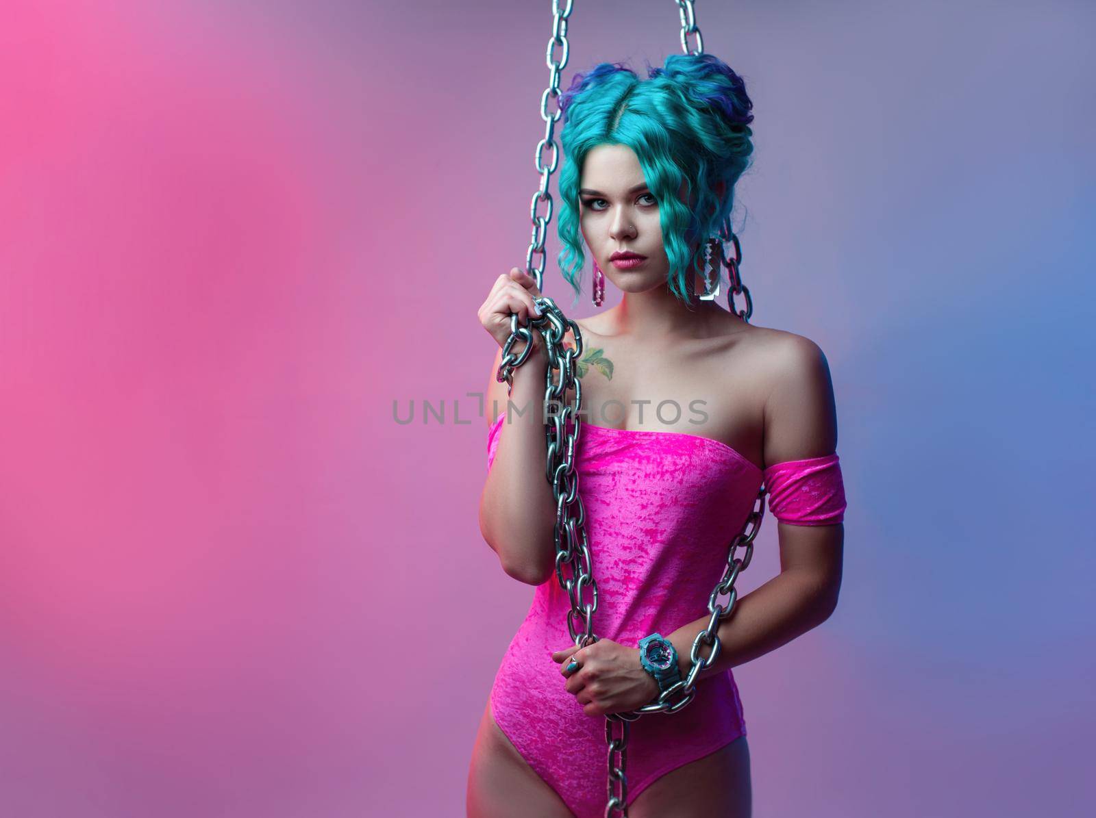 the sexy girl with colored hair in a bright pink bodysuit with a metal chain on a neon background