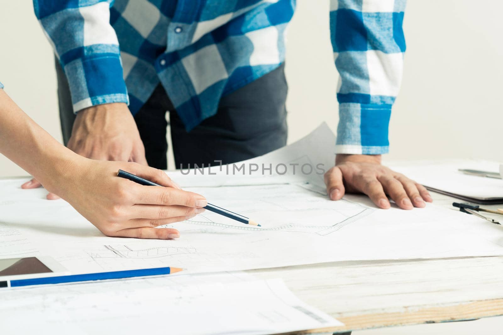 Design project discussing in architecture studio. Architect analyzing paper blueprint. Close up man hand pointing with pencil on construction drawing. Professional building, engineering and renovation