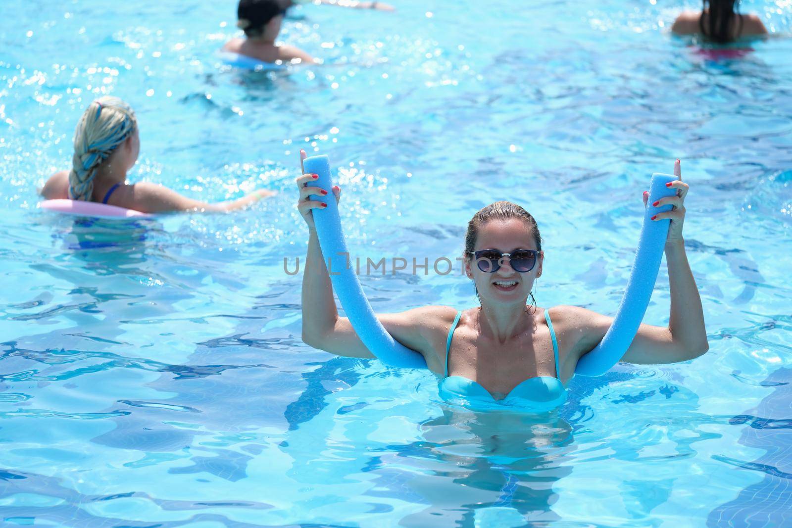 Happy smiling fitness woman exercising in noodle pool by kuprevich