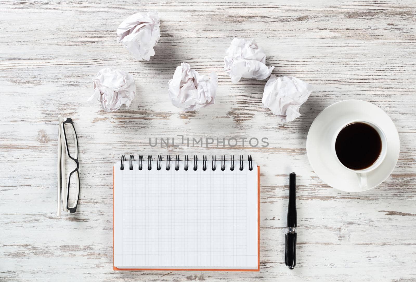 Still life of manager workplace in office with crumpled paper balls. Flat lay wooden desk with blank notebook and cup of coffee. Creativity and idea generation. Brainstorming meeting in design studio.