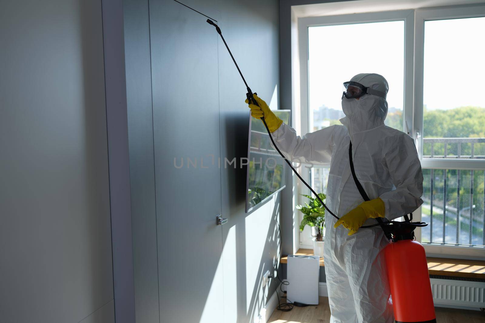 Worker in protective suit and face mask sprays chemicals indoors by kuprevich