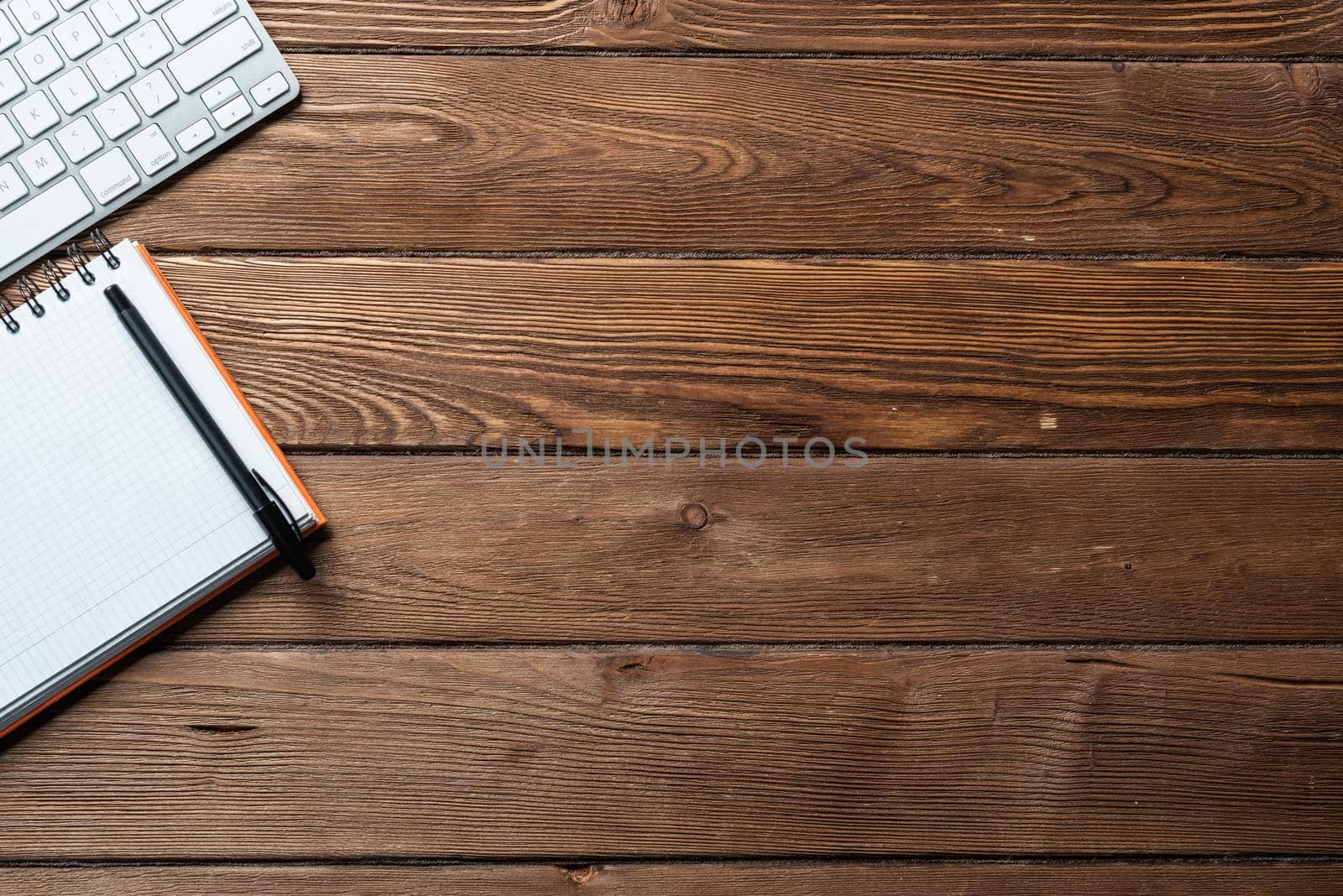 Top view of modern businessman workplace. Spiral notepad and computer keyboard on brown wooden surface. Education, creativity and innovation concept with copy space. Flat lay vintage office workspace