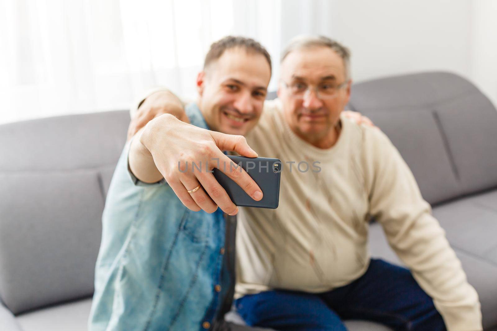 Happy moment. Cheerful young man taking a selfie with his upbeat elderly father waving at the camera and smiling pleasantly