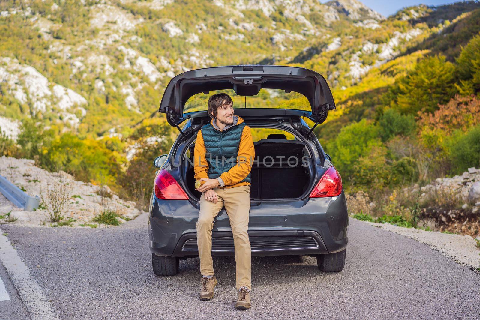 Young man traveler sitting on hatchback car with mountain background in evening time.copy space.