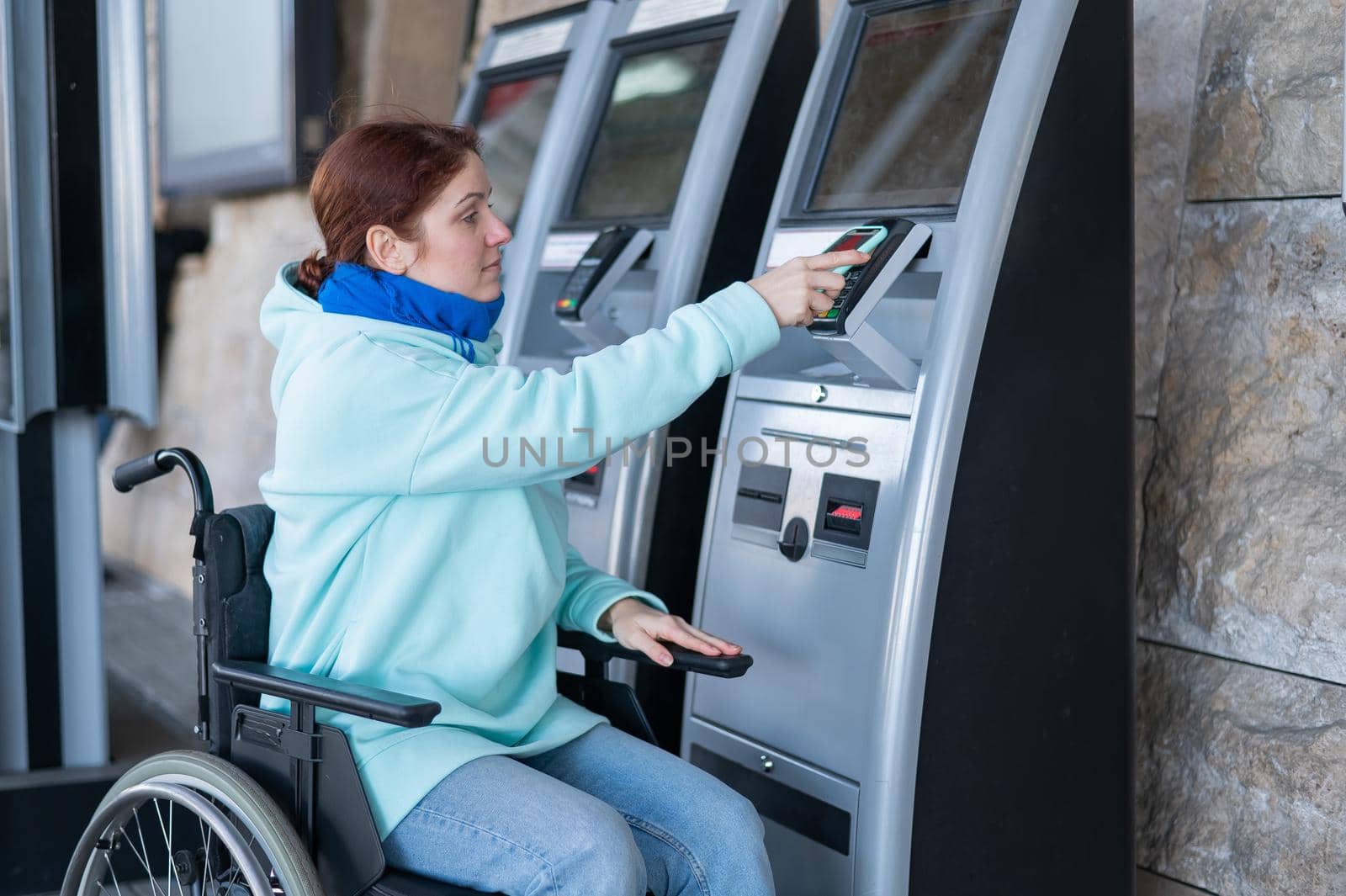 Caucasian woman in a wheelchair buys a train ticket using a mobile phone at a self-service checkout. by mrwed54