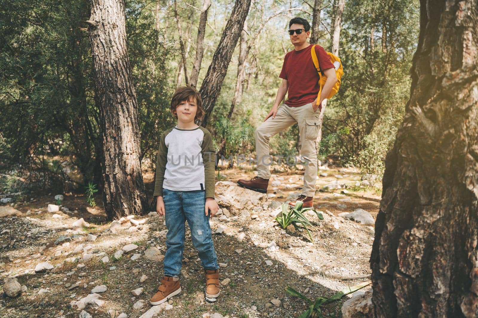 Tourists school boy and his dad walking in the spring forest. Child boy and father wearing casual clothes hiking in summer greenwood leaf forest. Family adventure in the woods.