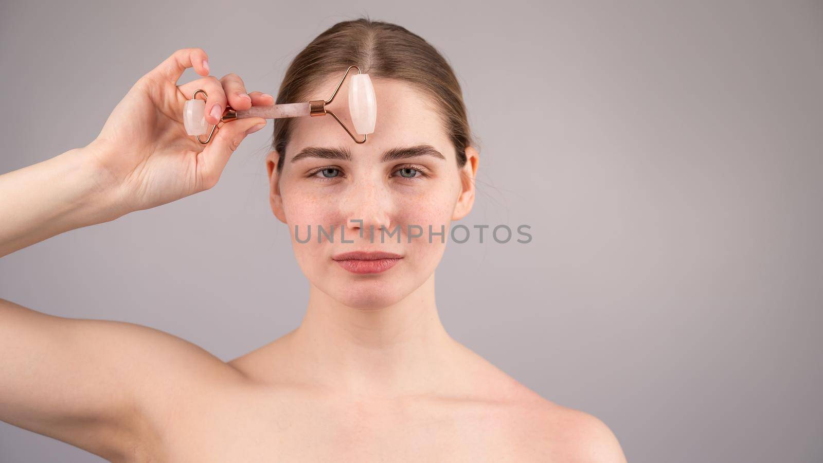 Close-up portrait of a woman uses a quartz roller massager to smooth wrinkles on her forehead