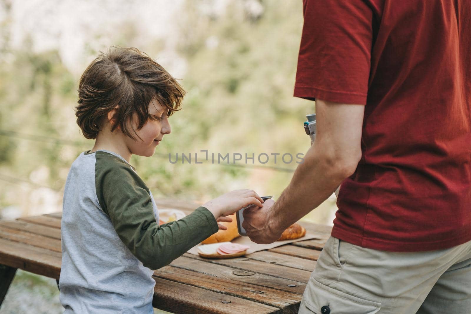 Close-up view of father and his school boy son on a family picnic in the mountains. Child kid and his dad taking a rest and enjoying a picnic while hiking in the mountains.