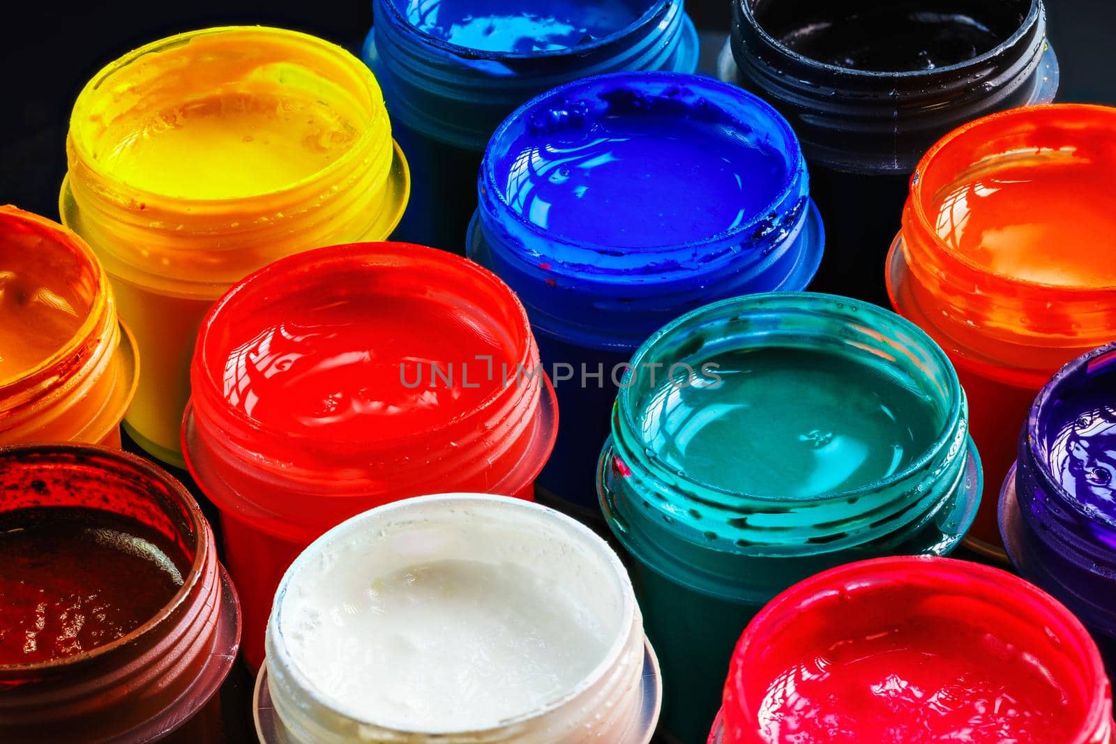 full-frame close-up background of opened small gouache paint jars on black