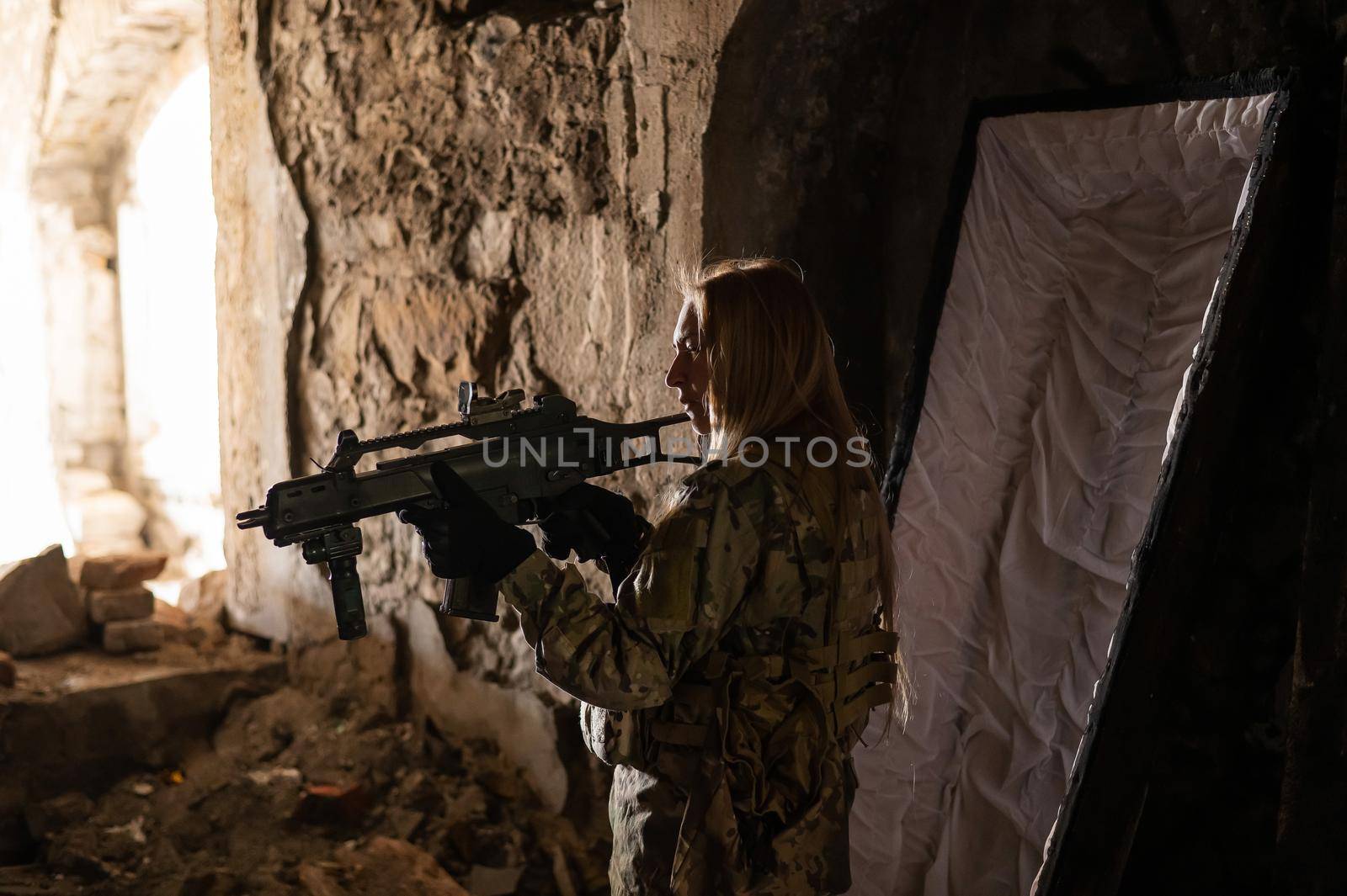 Caucasian woman in army uniform holding a machine gun and standing near an open coffin