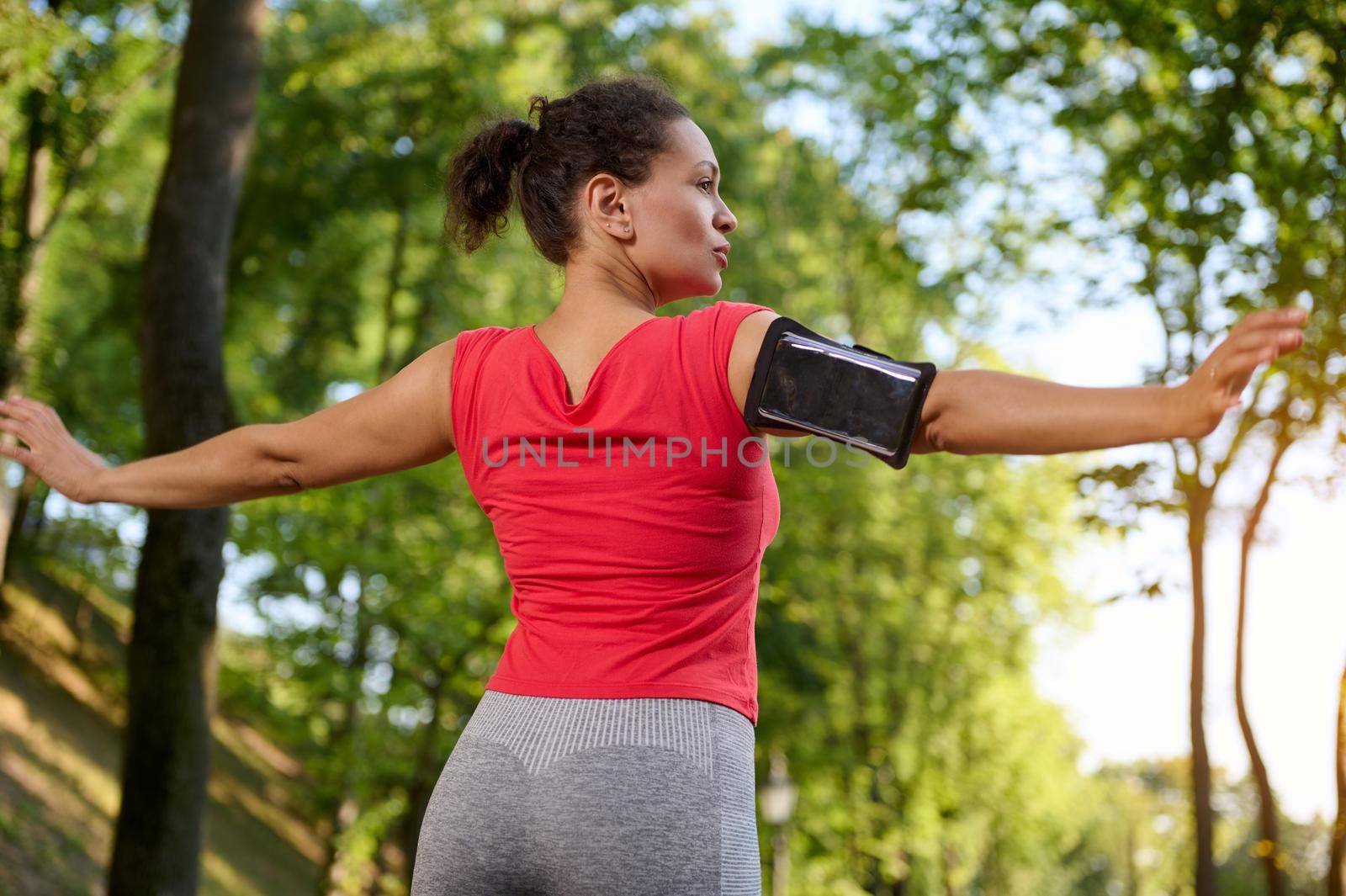 Confident beautiful fit woman stretching out, enjoying a morning cardio workout and relaxation exercises in the forest park on a summer sunny day by artgf