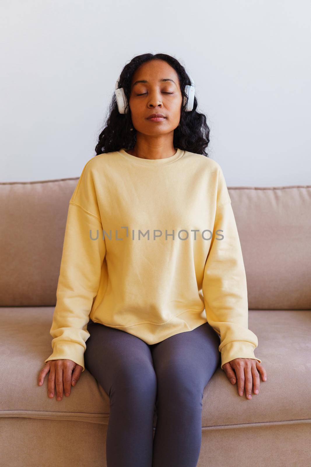 African-American woman sitting on sofa and listening to music in headphones. Concept of mindfulness and affirmative actions. Tranquil relax, calm meditation for personal fulfillment