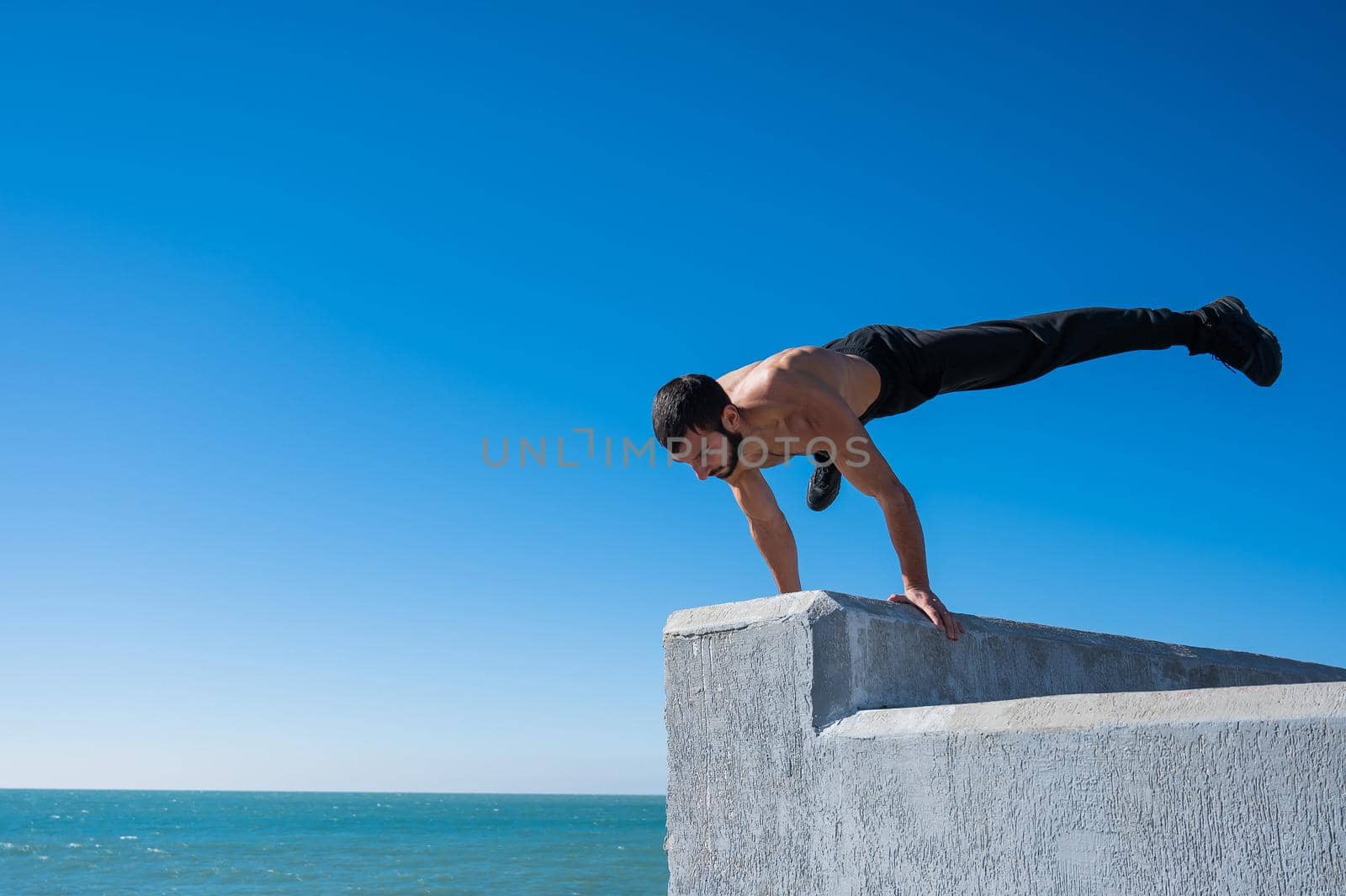 Shirtless man doing a handstand on a parapet by the sea