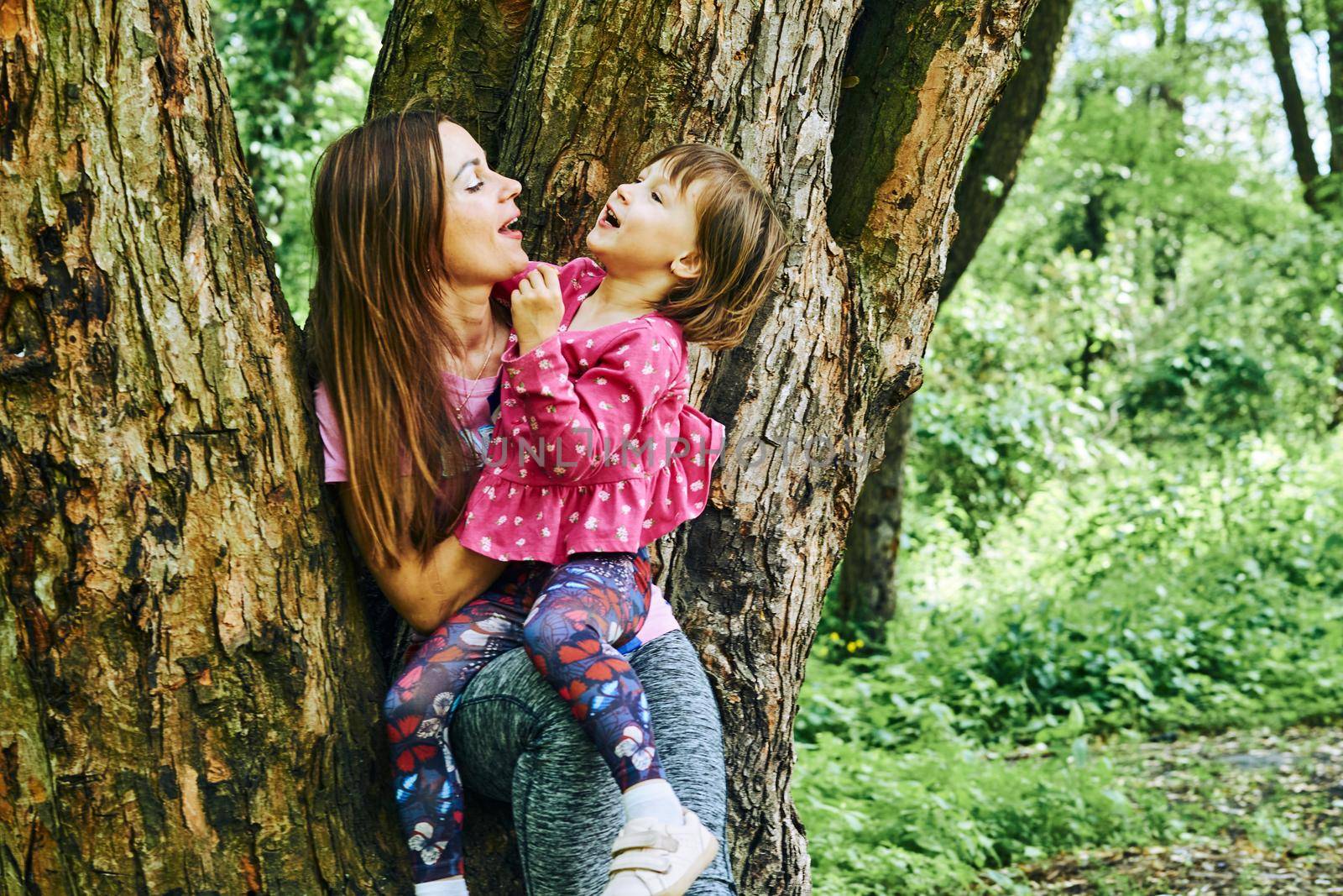 Cheerful mom with baby daughter near a big tree in a forest park by jovani68